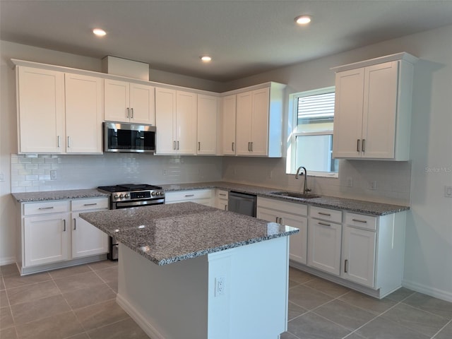 kitchen with white cabinetry, sink, a center island, light stone counters, and appliances with stainless steel finishes