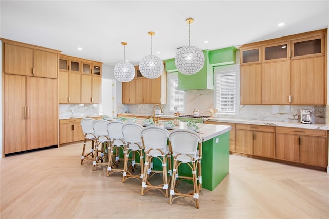 kitchen featuring hanging light fixtures, decorative backsplash, light parquet floors, a center island with sink, and a breakfast bar area