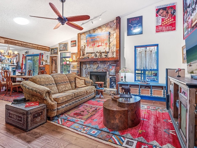 living room with ceiling fan with notable chandelier, a textured ceiling, vaulted ceiling, wood-type flooring, and a fireplace