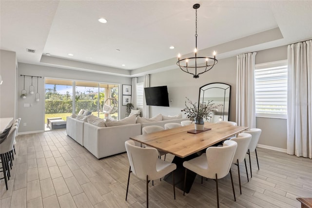 dining area featuring a tray ceiling, an inviting chandelier, and light wood-type flooring