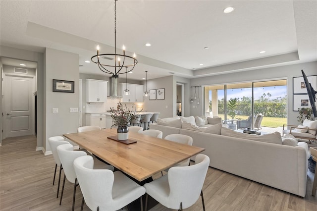 dining area with light hardwood / wood-style floors, a tray ceiling, and a notable chandelier