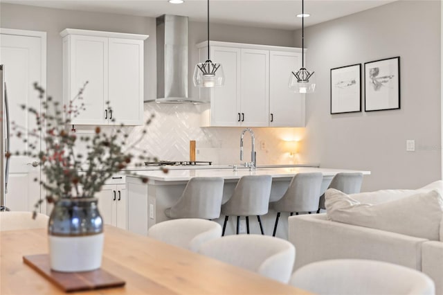 kitchen with backsplash, white cabinetry, pendant lighting, and wall chimney range hood