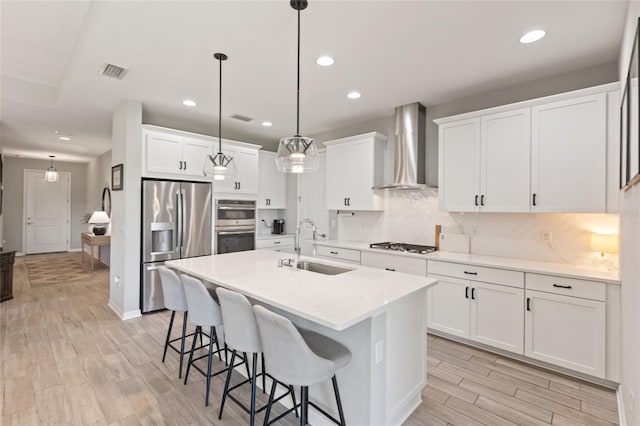 kitchen featuring stainless steel appliances, sink, wall chimney range hood, white cabinets, and hanging light fixtures