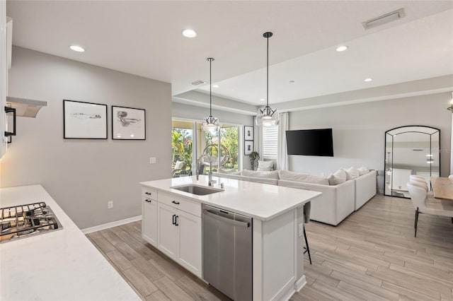 kitchen with a center island with sink, sink, appliances with stainless steel finishes, light hardwood / wood-style floors, and white cabinetry