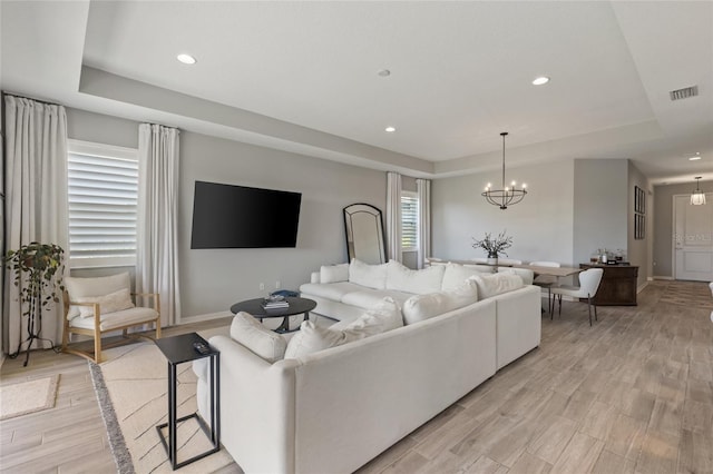 living room with light hardwood / wood-style floors, an inviting chandelier, and a tray ceiling