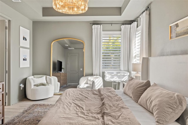 bedroom featuring a raised ceiling, light hardwood / wood-style floors, and an inviting chandelier