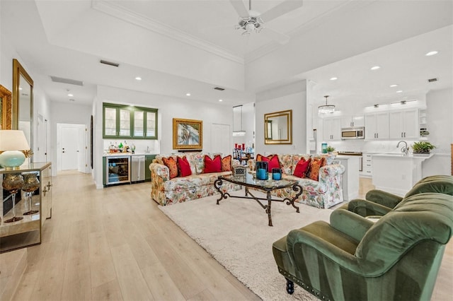 living room featuring ceiling fan, beverage cooler, wet bar, light wood-type flooring, and ornamental molding