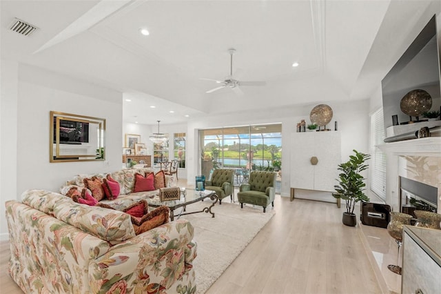 living room with light wood-type flooring, a raised ceiling, and ceiling fan