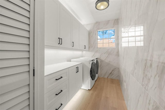 washroom with cabinets, independent washer and dryer, tile walls, and light hardwood / wood-style flooring