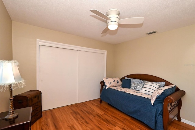 bedroom with a textured ceiling, a closet, hardwood / wood-style flooring, and ceiling fan