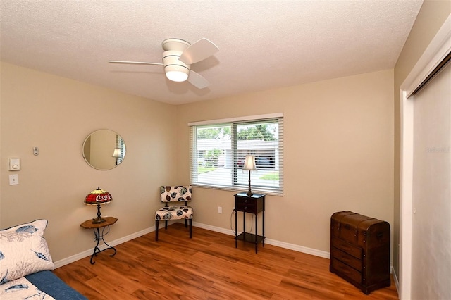 living area featuring hardwood / wood-style flooring, ceiling fan, and a textured ceiling