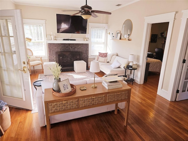 living room with a brick fireplace, ceiling fan, hardwood / wood-style flooring, and crown molding