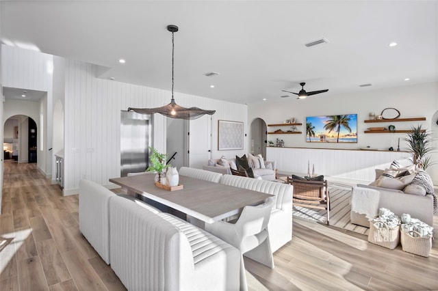 dining space featuring ceiling fan, wooden walls, and light wood-type flooring