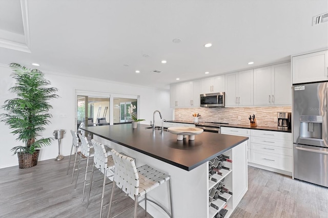 kitchen with stainless steel appliances, a kitchen breakfast bar, ornamental molding, white cabinets, and light wood-type flooring