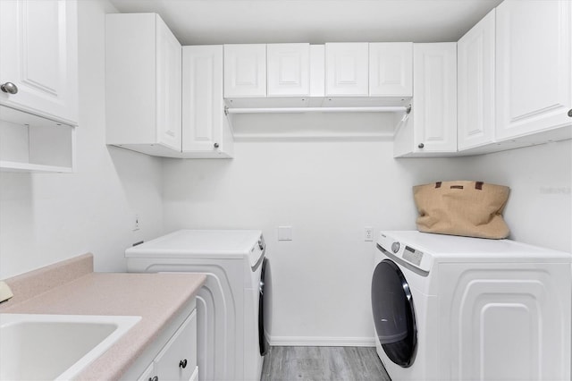 clothes washing area with washer and dryer, light hardwood / wood-style floors, cabinets, and sink