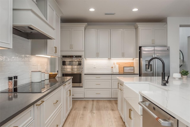 kitchen featuring decorative backsplash, white cabinetry, light wood-type flooring, stainless steel appliances, and custom range hood