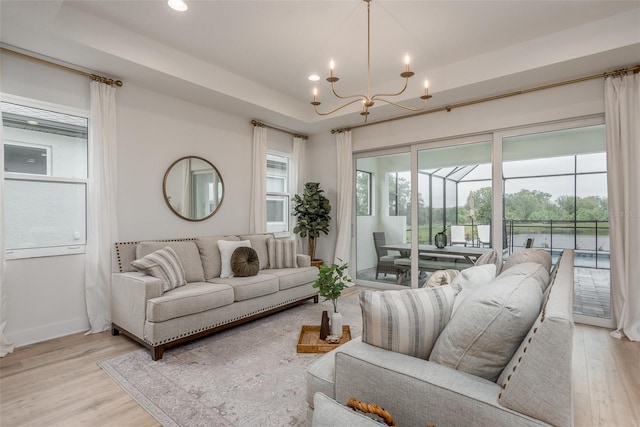 living room featuring light hardwood / wood-style floors, a raised ceiling, and an inviting chandelier