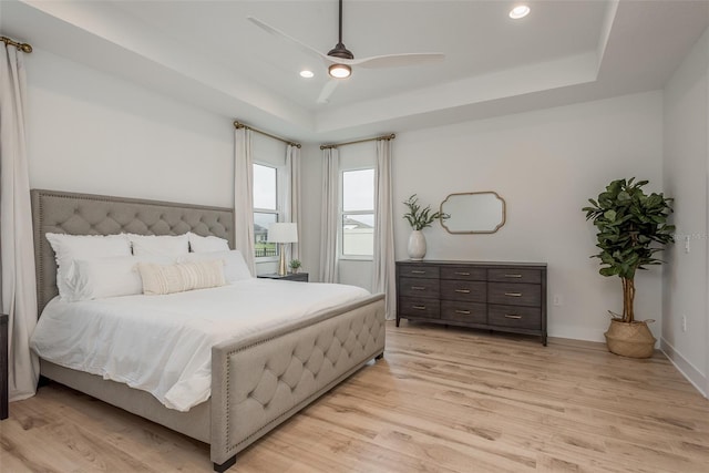 bedroom featuring ceiling fan, light hardwood / wood-style flooring, and a tray ceiling