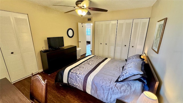 bedroom with a textured ceiling, dark hardwood / wood-style floors, ceiling fan, and multiple closets