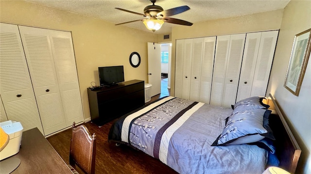 bedroom featuring a textured ceiling, two closets, ceiling fan, and dark wood-type flooring