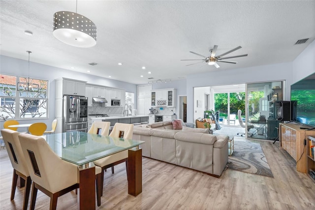 dining space with sink, ceiling fan, a textured ceiling, and light wood-type flooring