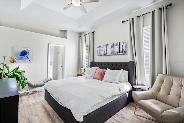 bedroom with ceiling fan, a tray ceiling, and light wood-type flooring