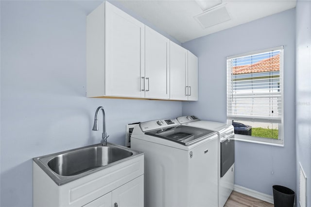 clothes washing area featuring cabinets, sink, washer and clothes dryer, and light hardwood / wood-style flooring