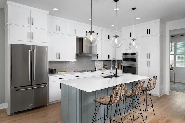 kitchen with appliances with stainless steel finishes, sink, wall chimney range hood, decorative light fixtures, and light hardwood / wood-style flooring