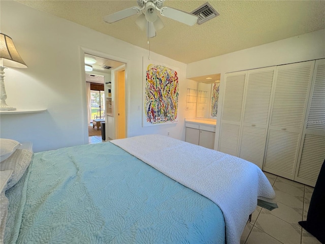 bedroom featuring ensuite bath, a textured ceiling, ceiling fan, a closet, and light tile patterned flooring