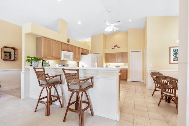 kitchen featuring a breakfast bar, white appliances, ceiling fan, light tile patterned floors, and high vaulted ceiling