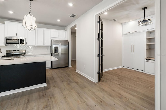 kitchen with white cabinets, decorative light fixtures, appliances with stainless steel finishes, and light hardwood / wood-style flooring