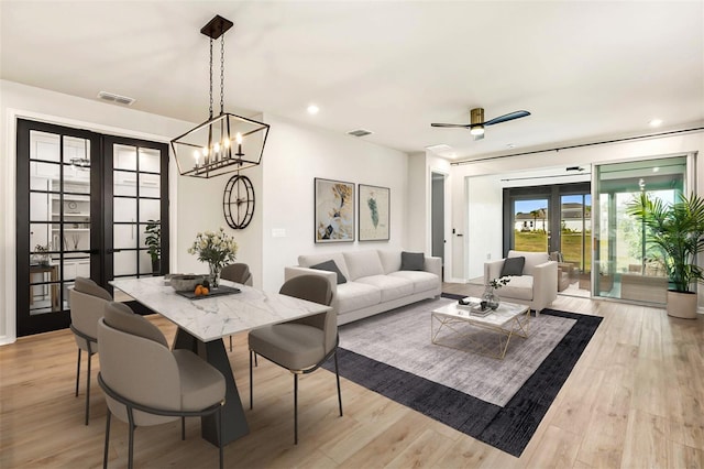 dining space with ceiling fan with notable chandelier, light wood-type flooring, and french doors