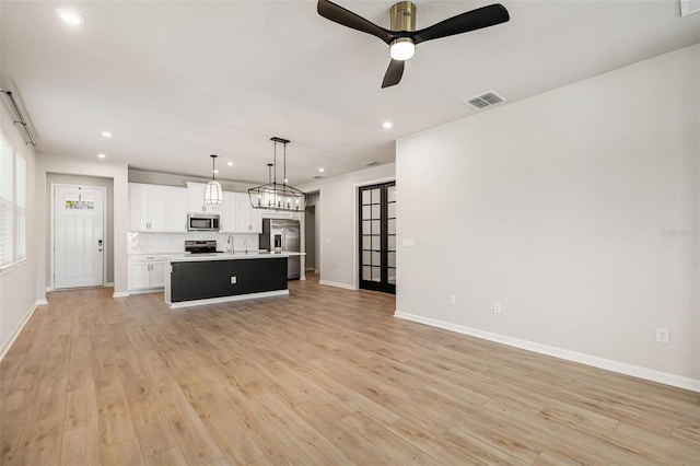 kitchen featuring hanging light fixtures, light wood-type flooring, an island with sink, appliances with stainless steel finishes, and white cabinetry