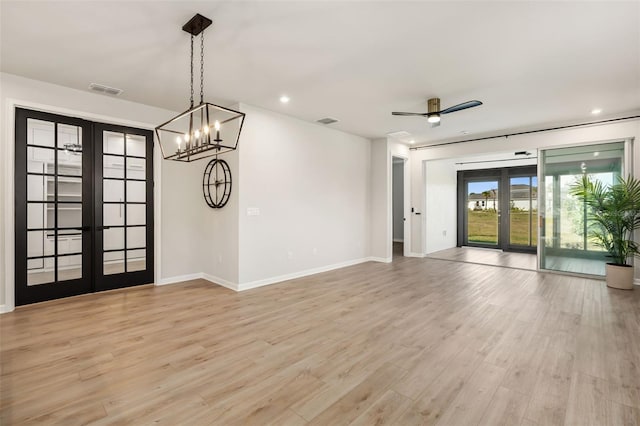 empty room with french doors, ceiling fan with notable chandelier, and light wood-type flooring