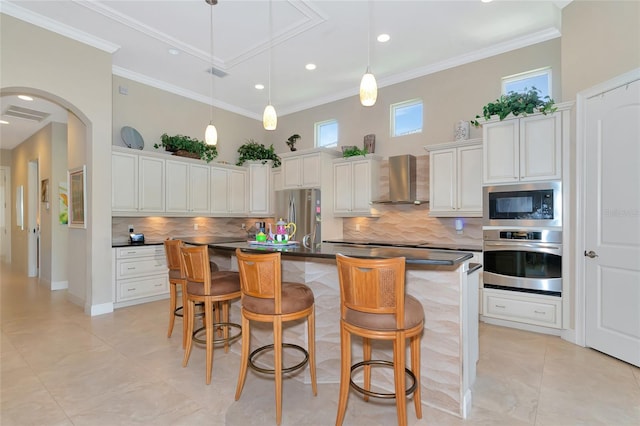 kitchen with a kitchen breakfast bar, wall chimney range hood, an island with sink, and appliances with stainless steel finishes