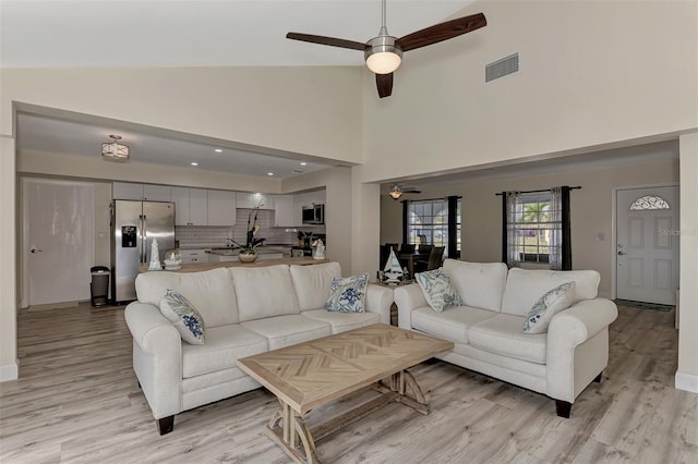 living room with ceiling fan, high vaulted ceiling, and light wood-type flooring