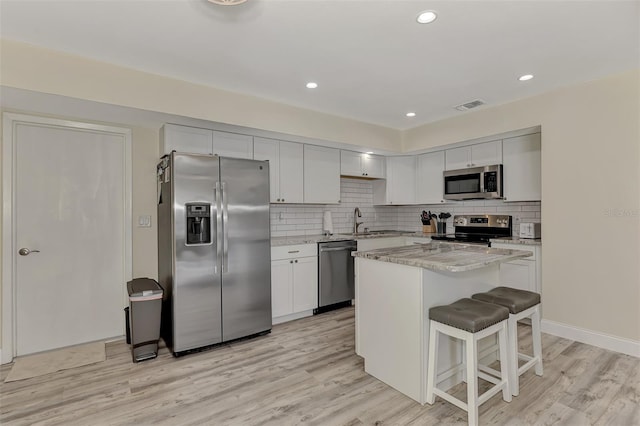 kitchen with a kitchen island, appliances with stainless steel finishes, a breakfast bar area, white cabinets, and light wood-type flooring