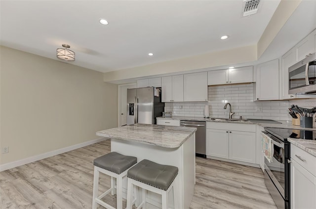 kitchen featuring sink, light stone countertops, light wood-type flooring, appliances with stainless steel finishes, and a kitchen island