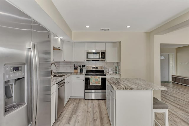 kitchen with white cabinetry, sink, light stone counters, appliances with stainless steel finishes, and light wood-type flooring