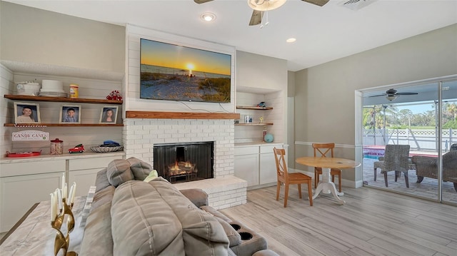 living room featuring light wood-type flooring, a brick fireplace, and ceiling fan