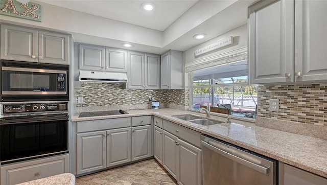 kitchen with sink, light stone counters, gray cabinets, decorative backsplash, and black appliances