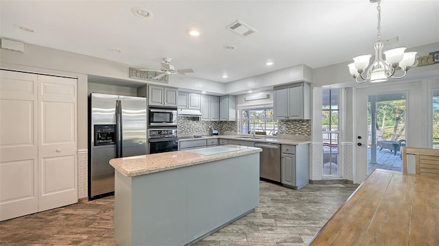 kitchen with appliances with stainless steel finishes, a center island, gray cabinets, and hanging light fixtures