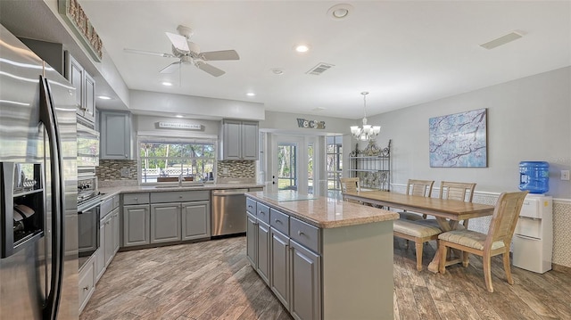 kitchen featuring appliances with stainless steel finishes, a center island, decorative light fixtures, and gray cabinetry