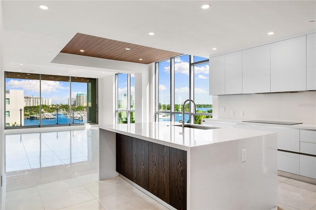 kitchen with a center island with sink, white cabinets, a water view, sink, and a wall of windows