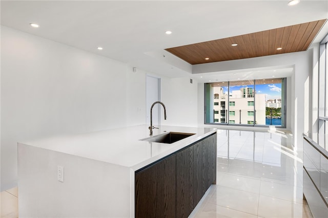 kitchen with sink, light tile patterned floors, an island with sink, dark brown cabinets, and wood ceiling