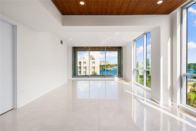 unfurnished room with a water view, a wall of windows, a healthy amount of sunlight, and wood ceiling