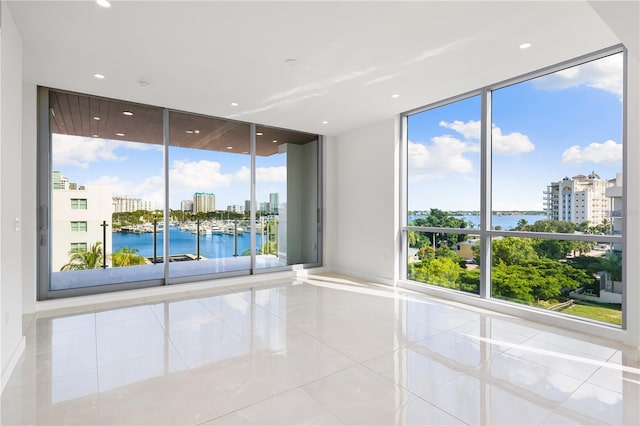 unfurnished room with floor to ceiling windows, a water view, and light tile patterned floors