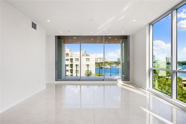 spare room with light tile patterned floors, a water view, and expansive windows