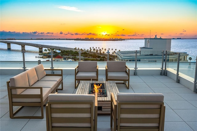 patio terrace at dusk featuring a water view and an outdoor living space with a fire pit