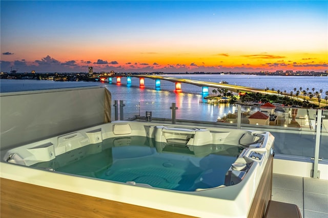 pool at dusk featuring a water view and a hot tub